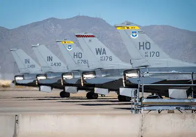 Military jets lined up on a runway with mountainous backdrop.