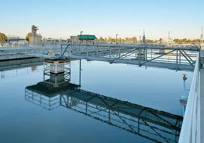 Water treatment facility tanks reflecting structures and sky at sunset.