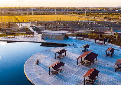 Outdoor pool area with shaded seating and sports fields in the background.