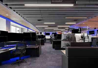 Modern office workspace with rows of desks and computers under bright ceiling lights.