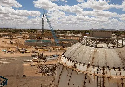 Construction site with cranes and large storage tanks under a cloudy sky.