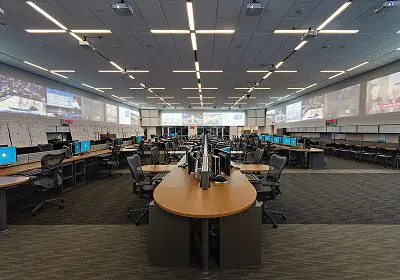 Modern open-plan office with rows of desks and ergonomic chairs under bright LED lighting.
