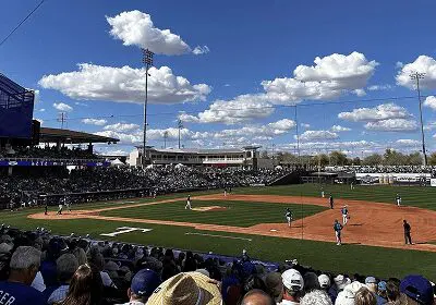 Baseball game underway at a sunny stadium with a crowd and blue sky.
