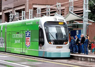 Modern green tram with NFL branding at a city stop.