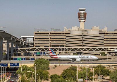 An American Airlines plane taxiing at an airport with terminal and control tower in the background.