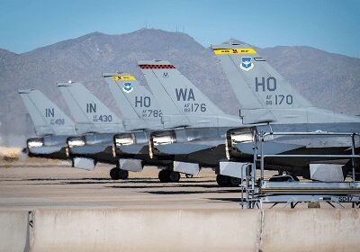 Military jets lined up on a runway with mountainous backdrop.