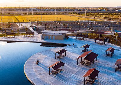 Outdoor pool area with shaded seating and sports fields in the background.
