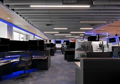 Modern office workspace with rows of desks and computers under bright ceiling lights.