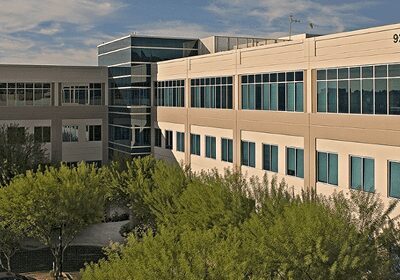 Modern office building surrounded by trees under a partly cloudy sky.