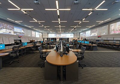 Modern open-plan office with rows of desks and ergonomic chairs under bright LED lighting.