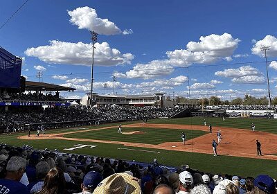 Baseball game underway at a sunny stadium with a crowd and blue sky.