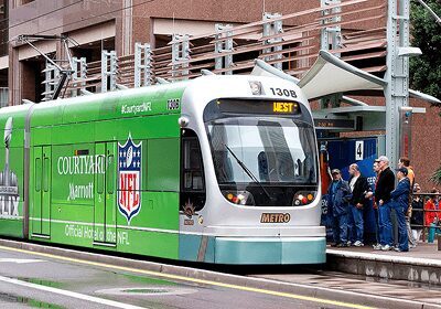 Modern green tram with NFL branding at a city stop.